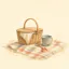Watercolour illustration of a picnic basket, a bucket and a spade on a checked blanket